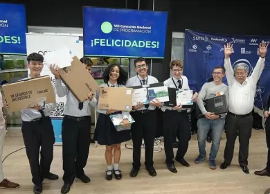 Grupo de estudiantes en uniforme escolar sosteniendo cajas de laptops con expresiones de alegría en un evento de entrega de equipos tecnológicos en un concurso en santander